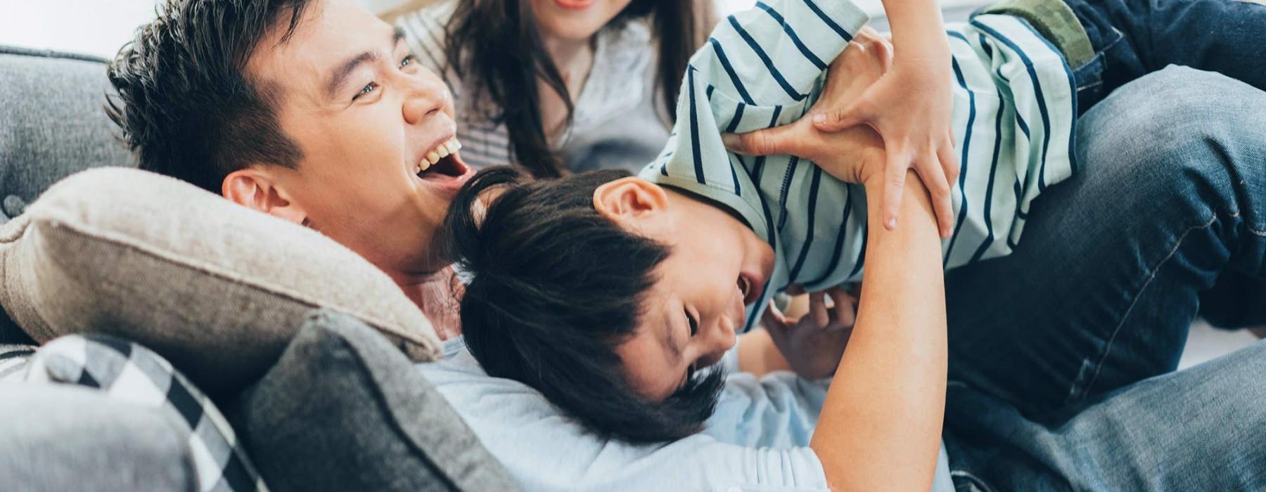 father plays on a couch with his young children